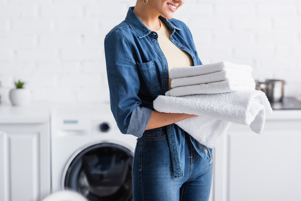 Vista recortada de ama de casa sonriente sosteniendo toallas limpias  - Foto, Imagen
