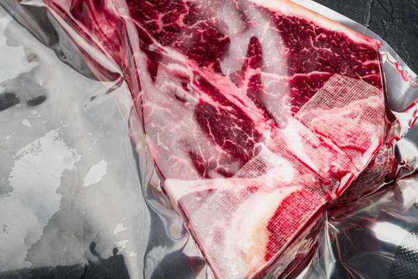 T-bone ή florentine dry aged raw marbled beef steak in vacuum packaging set, σε μαύρο πέτρινο φόντο, top view flat lay - Φωτογραφία, εικόνα