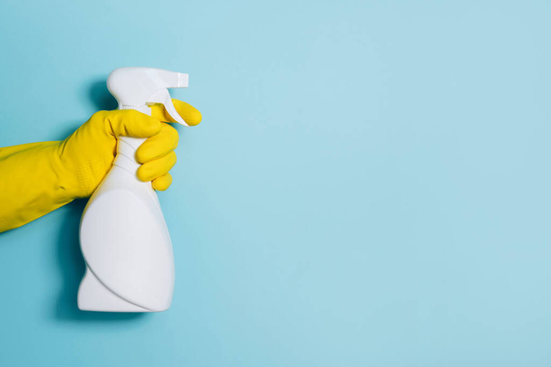 Hand in glove holding white plastic bottle of cleaning product, household chemicals. Copy space. Cleaning service concept. Household chemical cleaning products, brushes and supplies. Detergent bottle - Photo, image
