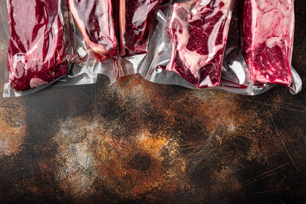 Beef steak vacuum set, tomahawk, t bone, club steak, rib eye and tenderloin cuts, op oude donkere rustieke achtergrond, bovenaanzicht vlak, met kopieerruimte voor tekst - Foto, afbeelding