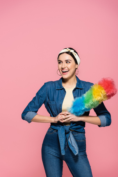 Positive housewife in headband holding dust brush isolated on pink - Foto, Bild