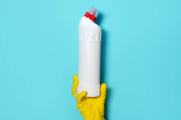 Hand in glove holding white plastic bottle of cleaning product, household chemicals. Copy space. Cleaning service concept. Household chemical cleaning products, brushes and supplies. Detergent bottle - Foto, Bild