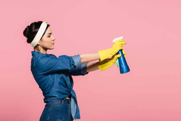 Vista lateral de la ama de casa sosteniendo detergente y trapo aislado en rosa - Foto, Imagen