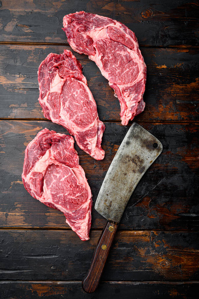 Syrové čerstvé mramorované maso Steak Ribeye Black Angus set, a starý řeznický nůž sekáček, na starém tmavém dřevěném stole pozadí, horní pohled plochý ležel - Fotografie, Obrázek