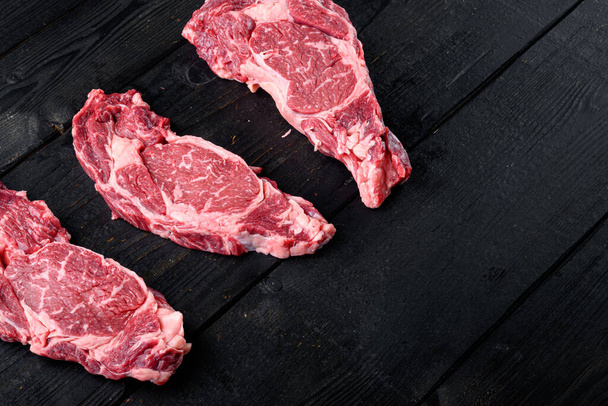 Surowe świeże marmurkowe mięso Steak Ribeye Black Angus zestaw, na czarnym drewnianym tle stołu, widok z góry płaski leżak, z miejsca na tekst - Zdjęcie, obraz