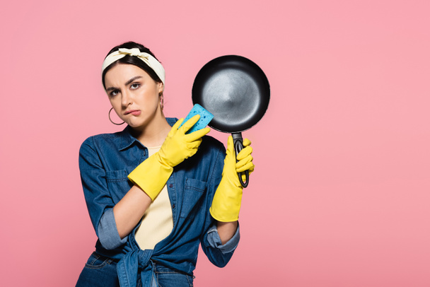 Housewife with sponge and frying pan biting lips isolated on pink  - 写真・画像