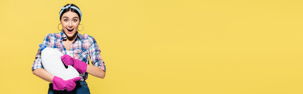 Podekscytowana gospodyni domowa trzymająca butelkę detergentu izolowaną na żółtym, sztandarze  - Zdjęcie, obraz
