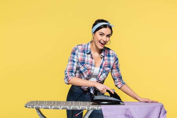 Smiling housewife ironing clothes isolated on yellow  - Photo, Image