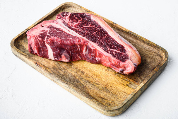 Roh frisches, trocken gereiftes Rindfleisch-T-Bone-Steak-Set, auf Holzplatte, auf weißem Steinhintergrund - Foto, Bild