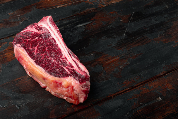 Sucho Zrající lub syrový steak připravený pro varnou sadu, na starém tmavém dřevěném stolku na pozadí, s kopírovacím prostorem pro text - Fotografie, Obrázek