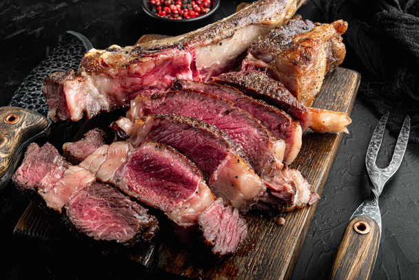 Tranches de steak de bœuf de viande marbrée grillée moyenne rare, coupées en tomahawk, sur une planche de service en bois, sur fond de pierre noire - Photo, image