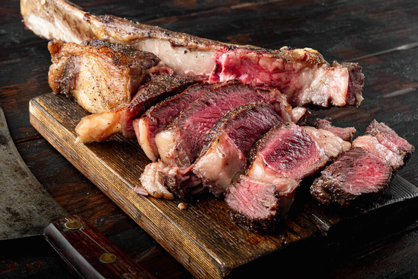 Grilled steak on the bone sliced, medium rare tomahawk cut set, on wooden serving board, on old dark  wooden table background - Photo, Image