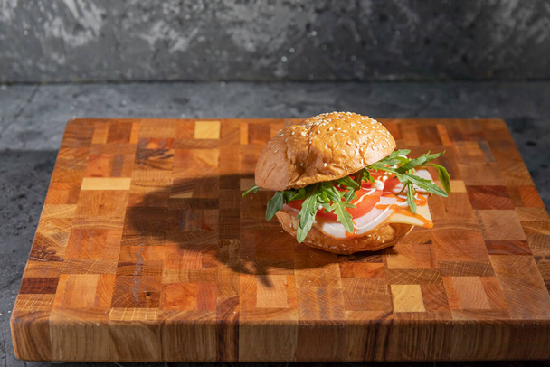 Сэндвич с ветчиной, рукколой, сыром и помидорами на разделочной доске. Селективный фокус. - Фото, изображение