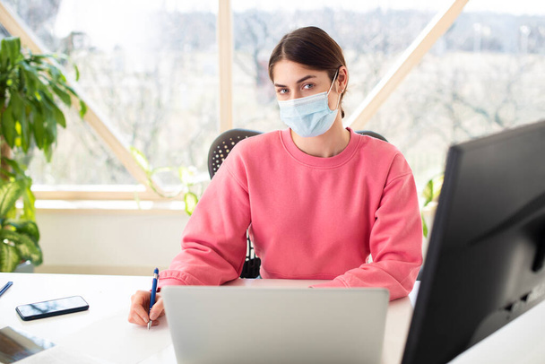 Shot of beautiful woman wearing face mask while sitting behind her computer and working. Home office.  - Foto, afbeelding