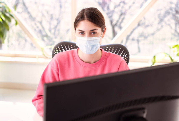 Shot of beautiful woman wearing face mask while sitting behind her computer and working. Home office.  - Fotografie, Obrázek