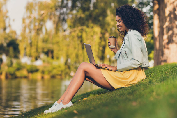 Photo of lady sit green grass hold netbook drink coffee wear yellow dress sneakers in green park outdoors - Fotografie, Obrázek