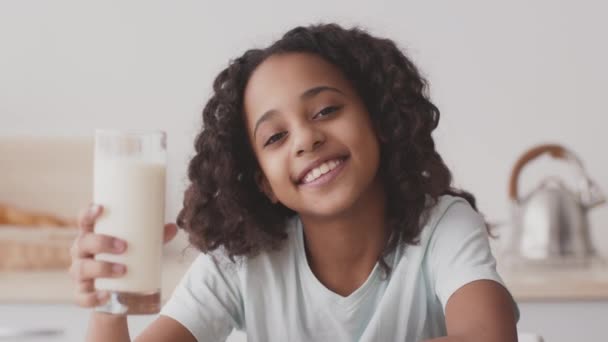 Benefici del calcio per i bambini. Ritratto di carina ragazza afro-americana felice che si gode il latte dal vetro e sorride alla macchina fotografica - Filmati, video