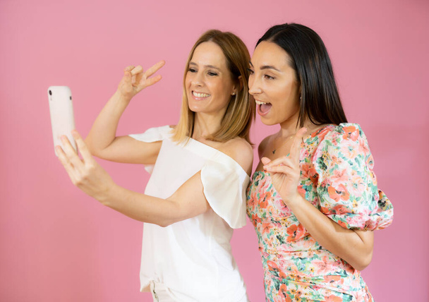 Δύο φίλοι που χρησιμοποιούν το κινητό τηλέφωνο σε ροζ φόντο. - Φωτογραφία, εικόνα