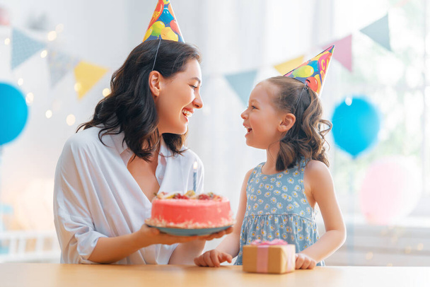 The kid is blowing out the candles on the cake. Mother and daughter are celebrating birthday. - Foto, imagen