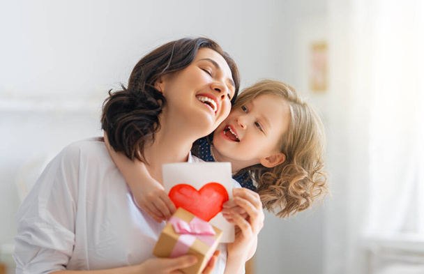 Happy mother's day! Child daughter is congratulating mom and giving her postcard. Mum and girl smiling and hugging. Family holiday and togetherness. - Zdjęcie, obraz