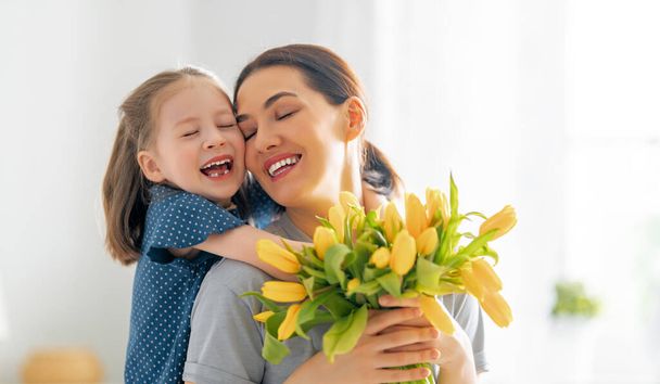 Happy mother's day. Child daughter congratulates mom and gives her flowers. Mum and girl smiling and hugging. Family holiday and togetherness. - Fotoğraf, Görsel