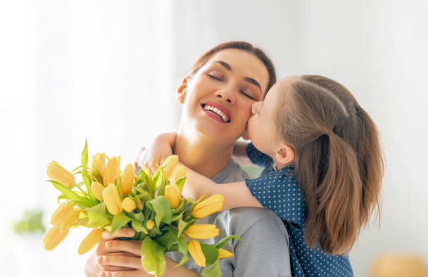 Happy mother's day. Child daughter congratulates mom and gives her flowers. Mum and girl smiling and hugging. Family holiday and togetherness. - Foto, Bild