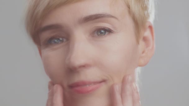 Primer plano borroso retrato de una hermosa mujer madura tocando su cara, disfrutando de su condición de piel facial - Metraje, vídeo