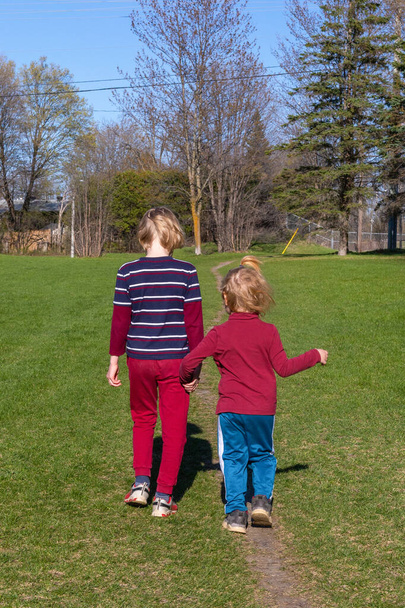 Dzieci spacerujące po parku wiosną. Rodzeństwo trzymające się za ręce. Koncepcja rodziny i przyjaźni. Brat i siostra razem od tyłu.. - Zdjęcie, obraz