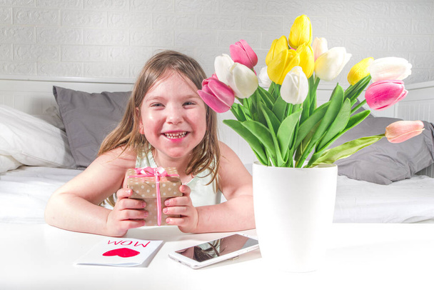 Mother's day, daughter's day holiday concept lifestyle. Preschooler child toddler blonde girl with a bouquet of tulip flowers, handmade greeting card and gift box copy space - Photo, Image