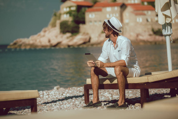 Чоловік розслабляється і використовує цифровий планшет на морському пляжі
 - Фото, зображення