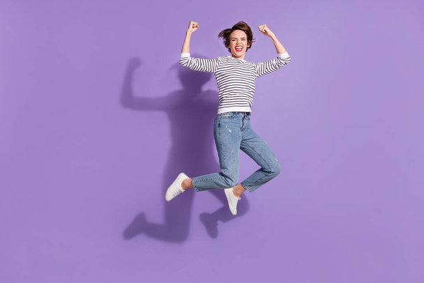Lunghezza completa foto di carino fortunato giovane donna indossare abbigliamento casual saltando pugni in aumento isolato colore viola sfondo - Foto, immagini