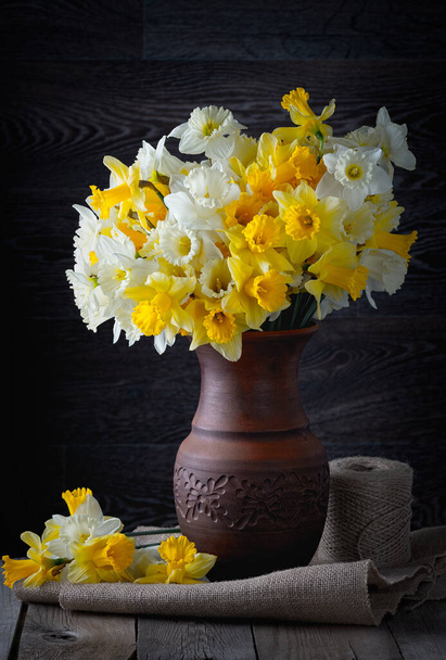 Frisse lente fel gele narcissen bloemen in een klei vaas op donkere achtergrond. Kopieerruimte. - Foto, afbeelding