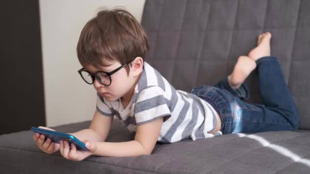 Neljä tonnia. pieni söpö valkoihoinen poika lasit tutkimuksessa puhelimessa - Materiaali, video