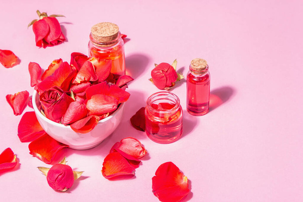 Lahvičky éterického oleje a okvětní lístky růží na růžovém pozadí. Módní tvrdé světlo, tmavý stín, místo pro text - Fotografie, Obrázek