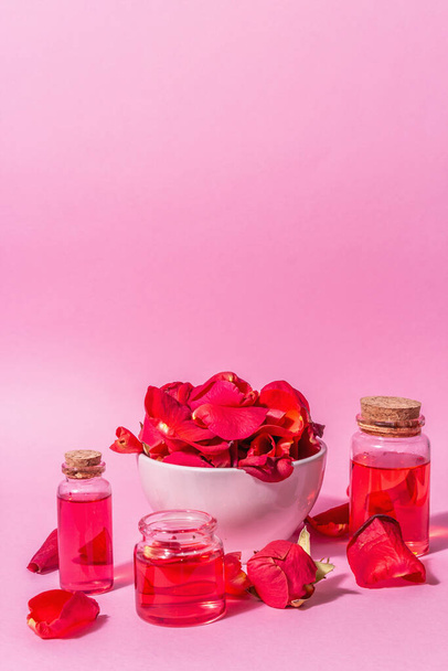 Bottles of essential oil and roses petals on pink background. Trendy hard light, dark shadow, place for text - Photo, image