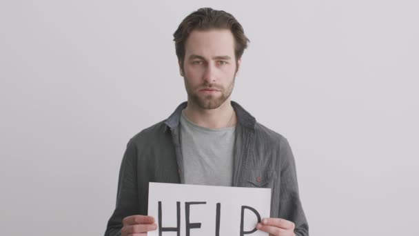 Unglücklicher junger süchtiger Mann hält Plakat mit Wort HILFE in der Hand und blickt traurig in die Kamera, fleht um Unterstützung - Filmmaterial, Video