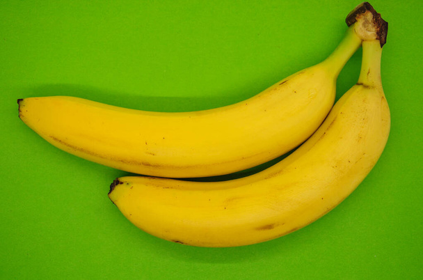 two yellow bananas on a green background. shadow and blur - Photo, Image