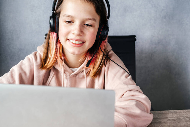 Gülümseyen kız kulaklık takıyor ve çevrimiçi, e-öğrenim ve çevrimiçi eğitim konsepti çalışırken bilgisayarını kullanıyor. - Fotoğraf, Görsel