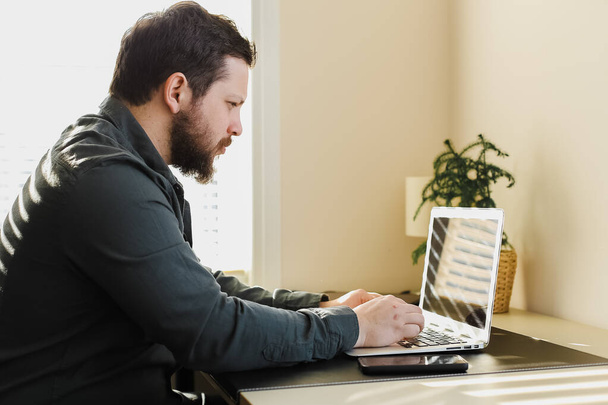Молодой бородатый бизнесмен работает в офисе, смотрит на экран ноутбука. - Фото, изображение