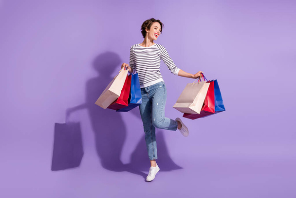 Full length photo of shiny buyer woman wear casual outfit dancing holding colorful shopping bags isolated violet color background - Fotoğraf, Görsel