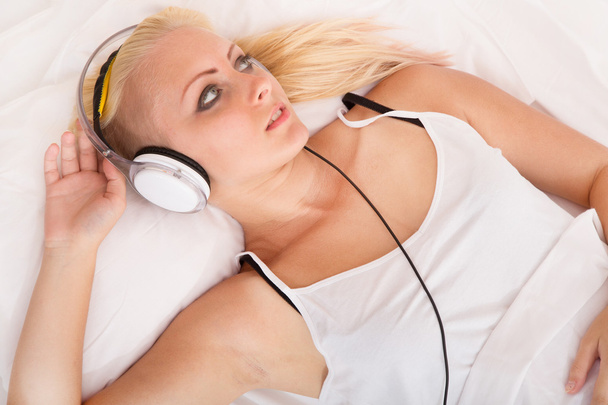Blonde girl lying in bed listening to music - Foto, imagen