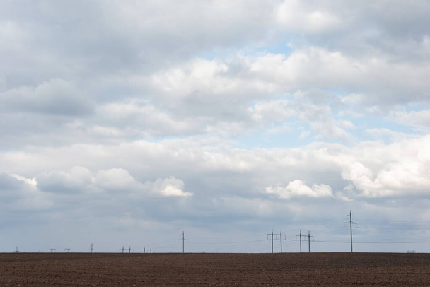 minimalistic landscape of a plowed field and clouds against the background of high-voltage towers. - Valokuva, kuva