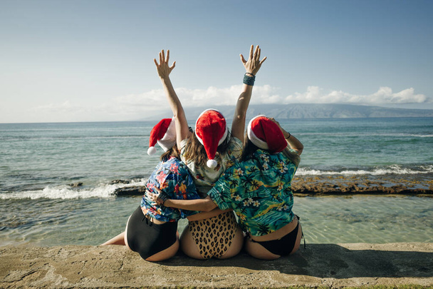 Κορίτσια με χαβανέζικα πουκάμισα κάθονται στην παραλία τα Χριστούγεννα στην Χαβάη. Υψηλής ποιότητας φωτογραφία - Φωτογραφία, εικόνα