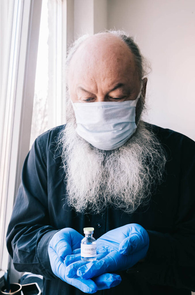 Vaccination Covid-19 pour les personnes âgées. Portrait d'un homme âgé barbu portant un masque médical et tenant une ampoule avec un vaccin contre le coronavirus. - Photo, image