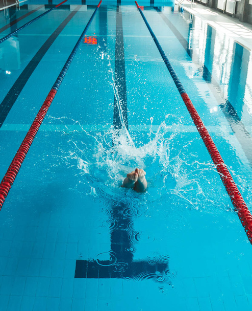 The swimmer pushes off the edge of the swimming pool. woman athlete jumps into the water indoors. Stopping in motion. View from the back. - Foto, Bild