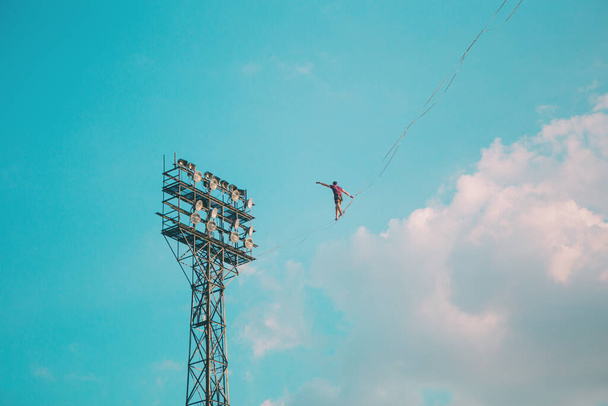 Highliner on a background of blue sky. A man walks along a sling stretched between the towers. The performance of the tightrope walker. A man is balancing over a precipice. A decisive step forward. - Photo, Image