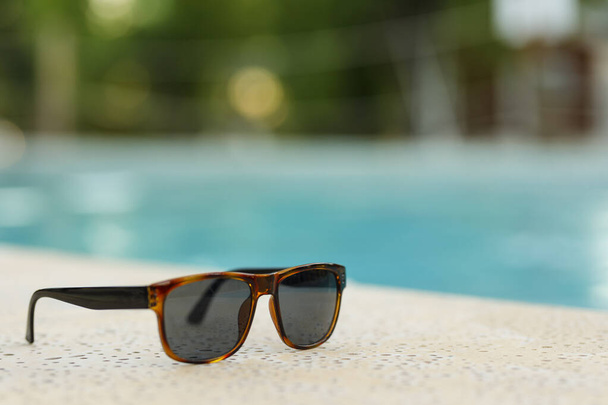 A summer holiday concept. Sun glasses near the swimming pool with crystal blue water. - Foto, Imagen