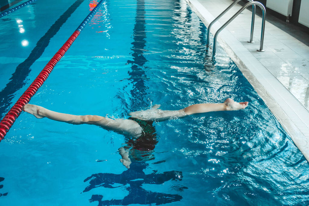synchronized swimming athlete trains alone in the swimming pool. Training in the water upside down. Legs peek out of the water. sports figure from legs. - Foto, Bild