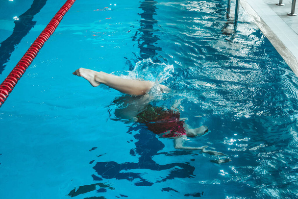 synchronized swimming athlete trains alone in the swimming pool. Training in the water upside down. Legs peek out of the water. sports figure from legs. - Φωτογραφία, εικόνα