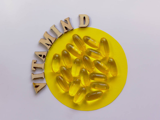 Keltaisia pillereitä tai tabletteja pienessä lautasella. D-vitamiini sanoja vuorattu puisilla kirjaimilla. Terveyskäsite. Tasainen lay, kopioi tilaa. - Valokuva, kuva